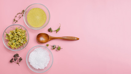 Fototapeta na wymiar Close up of Ingredients of ayurvedic treatment or face pack. Yellow clay, turmeric powder and dried chamomile, sea coarse salt in glass cups on a pink pastel colour background. Flat lay blog style