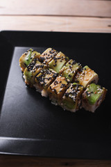 Salmon sushi on a square black plate on a dark wooden background