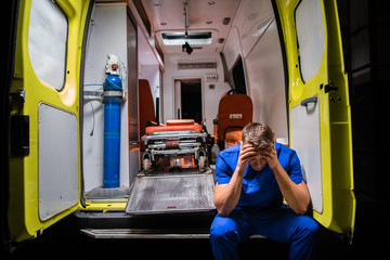 Confused paramedic in a blue uniform sitting in the back of an ambulance car