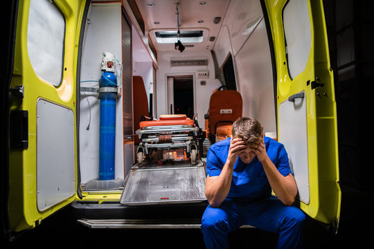 Confused paramedic in a blue uniform sitting in the back of an ambulance car