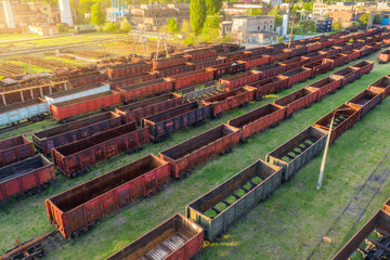 Aerial view of freight trains. Top view of old rusty wagons on railroad. Heavy industry. Industrial landscape with train, green trees and grass at sunset in summer. Railway station. Transportation