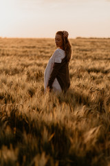 Young beautiful pregnant woman in white dress walking in the wheat orange field on a sunny summer day. Nature in the country. Miracle expectation. Sunset on isolation