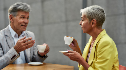 Coffee break. Stylish mature couple enjoying coffee and talking to each other while sitting at cafe outdoors