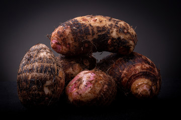 Couple of hairy brown pink raw Yam edible vegetable from the local Brazilian market against a dark grey background. Studio low key food concept still life. - obrazy, fototapety, plakaty