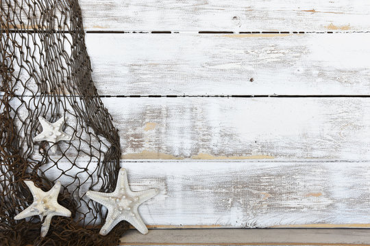 An image of three white decorative starfish and fishing net on an old white washed wooden background. 