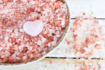 Fototapeta na wymiar A top view image of organic pink Himalayan salt with rose quartz crystal on an old white wooden table top. 