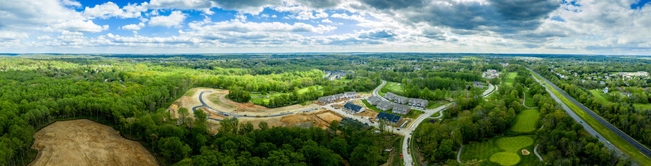 Fototapeta na wymiar Aerial panorama of large construction site of a new single family home and town house neighborhood in the middle of a golf course in Turf Valley Maryland with home sites and triplexes