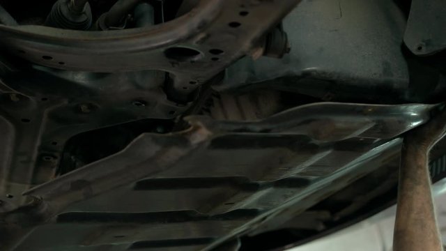 Installing crankcase protection by two auto mechanics. Close-up the car bottom. Car is lifted up at service station.