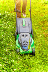 Man cutting green grass with lawn mower in backyard. Gardening country lifestyle background. Beautiful view on fresh green grass lawn in sunlight, garden landscape in spring or summer season.