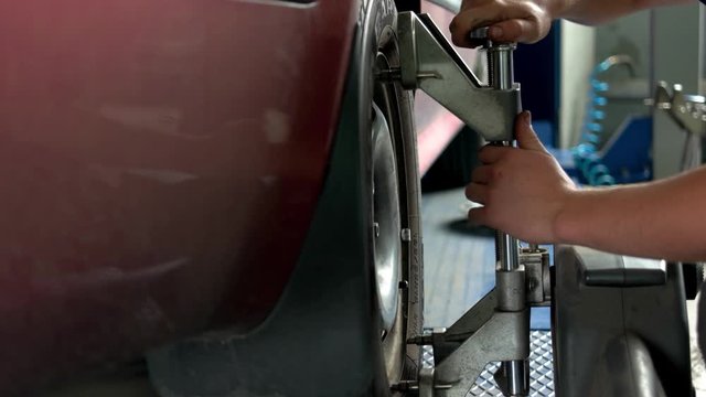 Engineer is setting camber caster gauge for checking alignment of tire. Close-up mechanic hands and car tool.