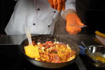 A chef with gloves in his hands adds spices to the pan with the cooking dish