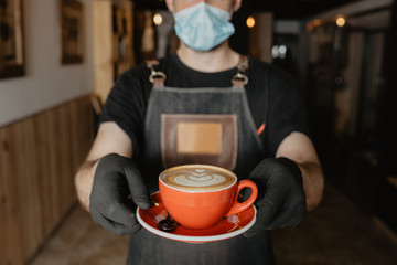 barista camarero con mascarilla y guantes está enseñando una taza roja de café con dibujo latte art