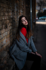 Girl in a red blouse and a gray cardigan on the background of the old brick wall