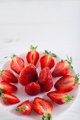 Juicy fresh sliced strawberries on a white plate on a white wooden background