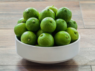 Green lemons in a white bowl on wood