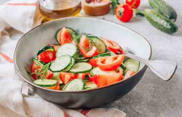 Healthy vegetable salad of fresh tomato, cucumber, dill and spices and oil in bowl on light gray background. Diet concept.