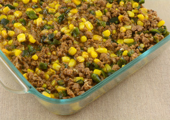 Layer of Mexican food casserole of corn kernels, chopped poblano peppers, and cooked ground pork in glass baking dish