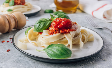 Pasta Tagliatelle Bolognese with meat tomato sauce and fresh basil leaves on white plate. Light gray table.
