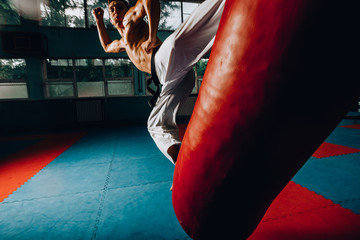 Fit karate man kicking at punching bag in the gym