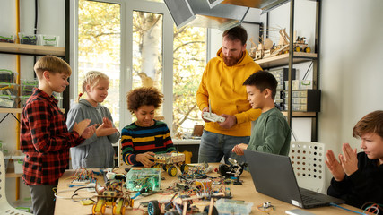 High performance. Young creative male teacher explains for students the principle of robotic machines work while holding console controller. Science and education.