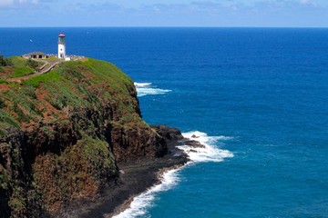 White Lighthouse set atop a cliff with a brilliant blue ocean in the background in Kauai, Hawaii, USA.