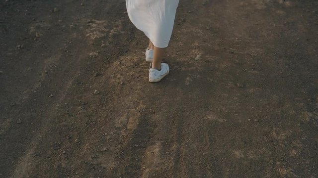 A girl walks along the summer island during sunset. Legs of a girl in beauties and a long white dress walk on mountains, stones. Atmospheric video