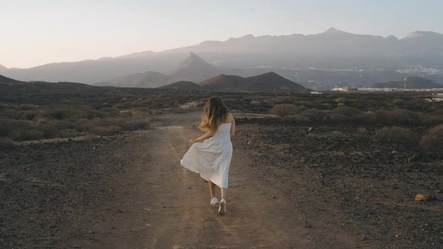 A girl in a white long dress runs on a journey, dances, enjoys nature, freedom. Long-haired beauty in the mountains against the sunset. The beauty of the islands