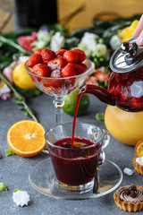 The process of brewing natural tea with strawberries, tea ceremony. A cup of freshly brewed fruit tea. Hot tea is poured into a glass cup on a decorative background