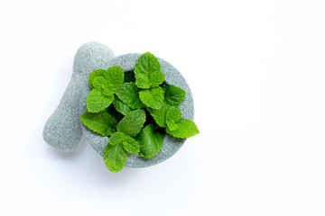 Mint leaves in stone mortar and pestle on white background.