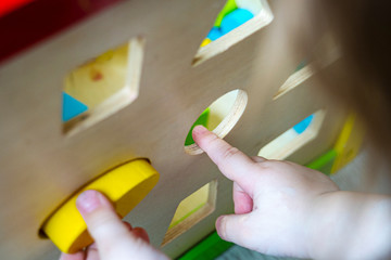 Hands of the little girl shove a figure of yellow oval in the hole of a wooden sorter. early learning concept