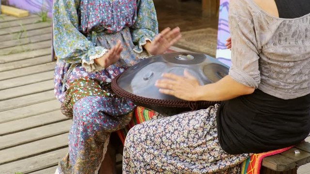 Two girls play the tank drum or hang on ethnic open air concert. Relaxation, folk, meditative and traditional ethnic music concept. Hands close-up, 4K