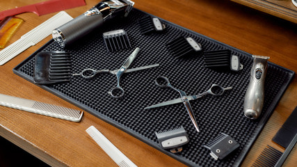 Barber tools. Scissors, combs for hair and beard, hair clipper are lying on a rubber mat in the barber shop. Top view. Web banner