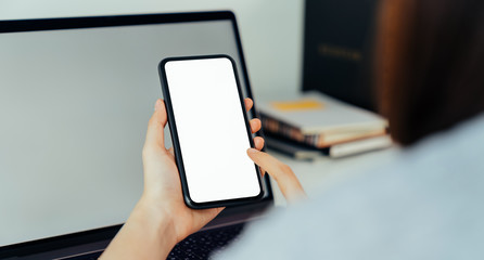 Woman hand holding smartphone with blank copy space screen for your advertisement. laptop on the table.
