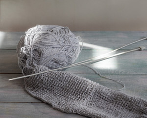 Knitted blank from gray yarn of gray color, a ball of yarn and knitting needles for knitting on a wooden background