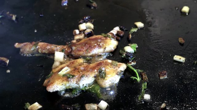 Frying chicken on black gridle with olive oil and green spring onions.