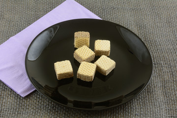 Bite size chocolate hazelnut wafer cookies on black dessert plate with lavender napkin