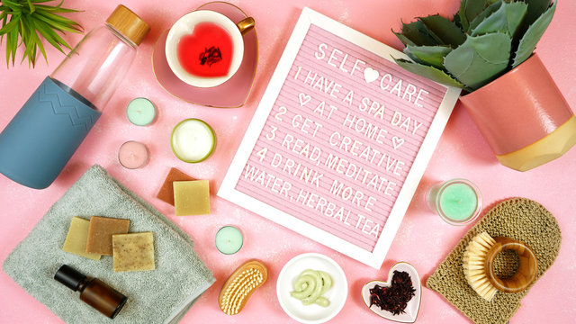 Self-care wellbeing home spa letterboard with herbal hibiscus tea, pro environmental plastic free beauty products and moisturisers on feminine pink background.