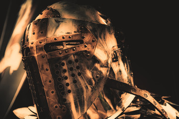 Shiny medieval iron knight helmet with a golden cross, full of scratches due to battles with...