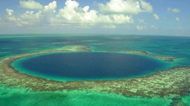Aerial: Large marine sinkhole with yacht in sea against sky, drone descending over seascape on sunny day - Great Blue Hole, Belize