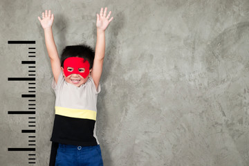 The boy in the superhero outfit smiled and raised his hand to show the growth, with a unit beside him..Boy power concept and development of young children.