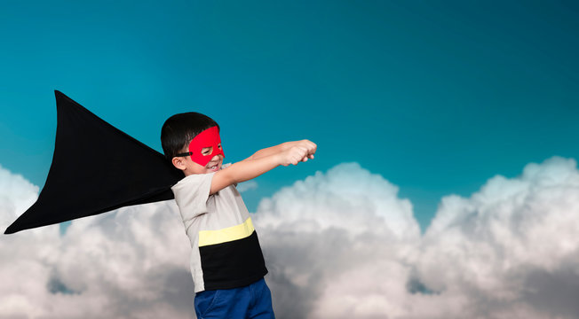 The boy dressed up in a superhero outfit, pretending to flying on the sky background.Study concepts And development of young children.