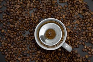 A cup of brewed coffee is served on roasted coffee beans.