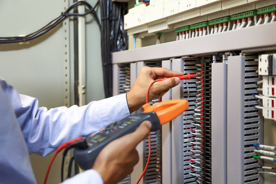 Electrical engineer using digital multi-meter to check current voltage at circuit breaker in main distribution board.