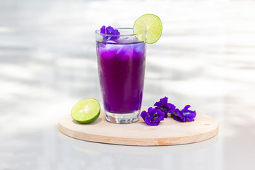 Butterfly pea juice with ice in transparent cup serve on Wooden sheet with flower and lemon (Clitoria ternatea).