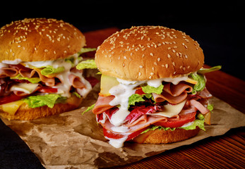 Sesame seeded sandwiches with fresh vegetables and ham on wooden board.