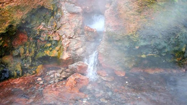Seamless loop cinemagraph of steam geyser in Deildartunguhver hot springs in Iceland with cloudy mist fog coming out of red rock colorful cave boiling water vapor