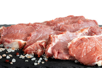 Fresh raw beef steaks on a black  slate plate isolated white background. Raw rib eye steak on a slate plate with salt and pepper.