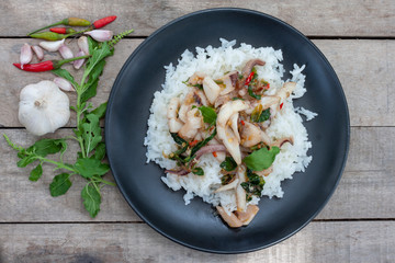 Top view of fried holy basil leave with squid on rice in black plate on wooden table.