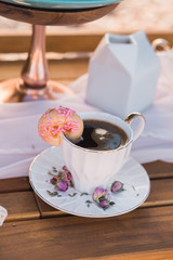 Pink donut on the side of a romatic cup of coffee
