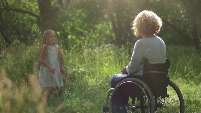 Mother in a wheel chair spend time together with her children and husband throwing a frisbee in a back yard or farm forest or park. Father with kids showing love and care to a mother. Family concept